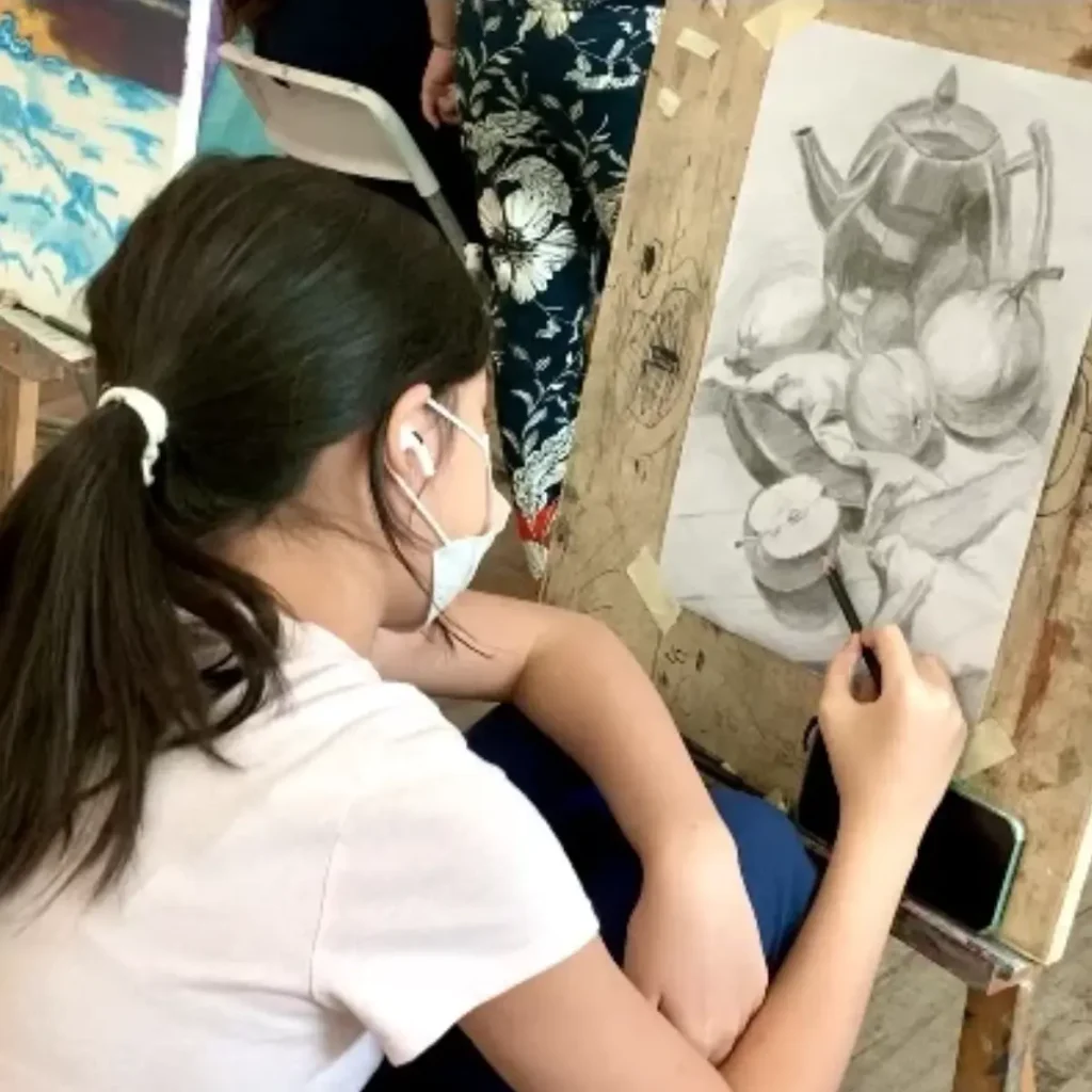 Youth sketching observational drawings of still life objects in art studio