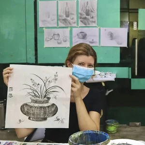 Student holding up ink painting board and brush during Chinese ink painting trial class session