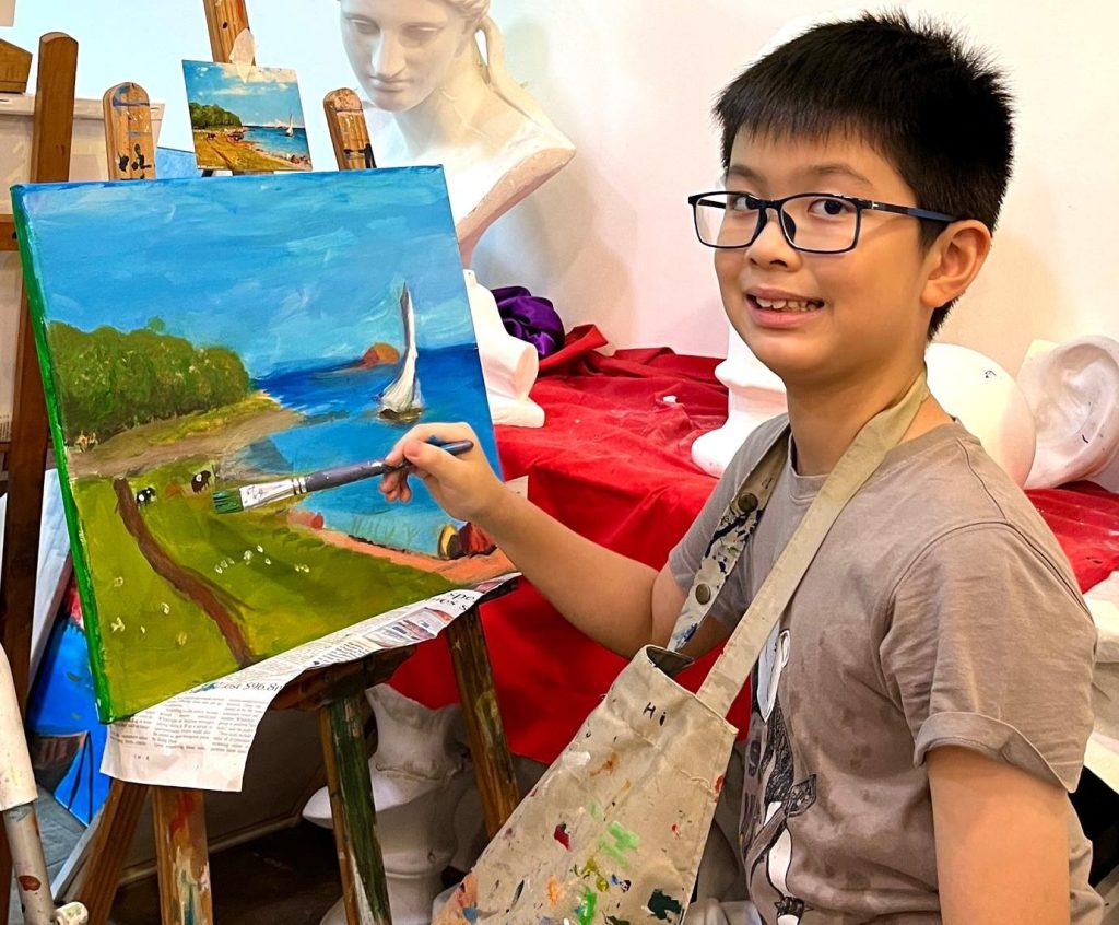 A boy finishing up his acrylic painting of a landscape, children kid finishing up his painting