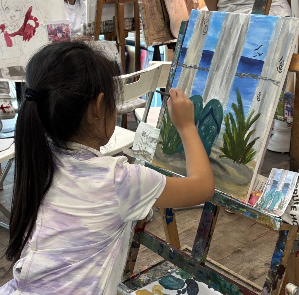 A girl doing a creative acrylic painting of some sandals on a beach in visual arts centre studio in our professional acrylic painting art course and art class art lesson