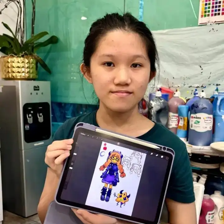 Student proudly holding up an iPad showing her digital drawing of an anime-style character, created during a digital art costume design class